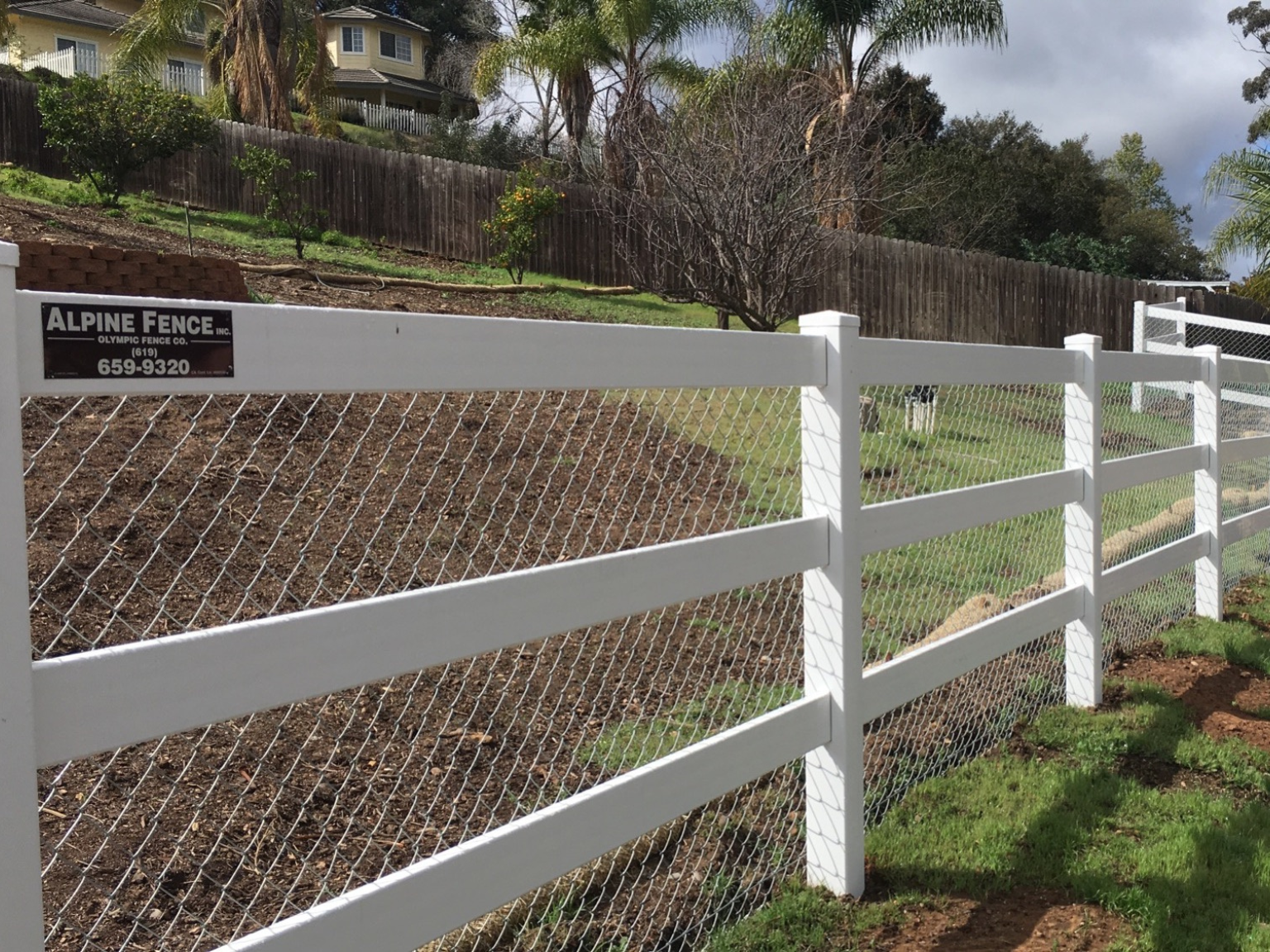 Vinyl ranch rail fence with galvanized chain link backing by Alpine Fence Company.