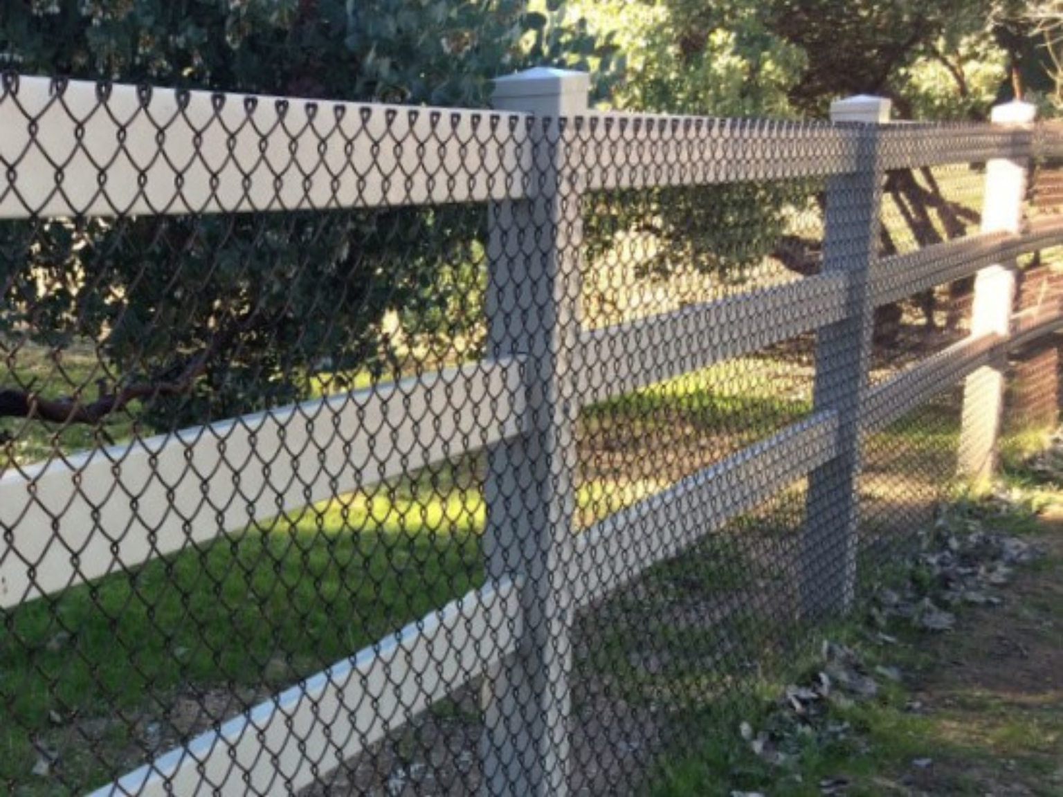 Tan vinyl ranch rail fence with chain link backing by Alpine Fence Company.