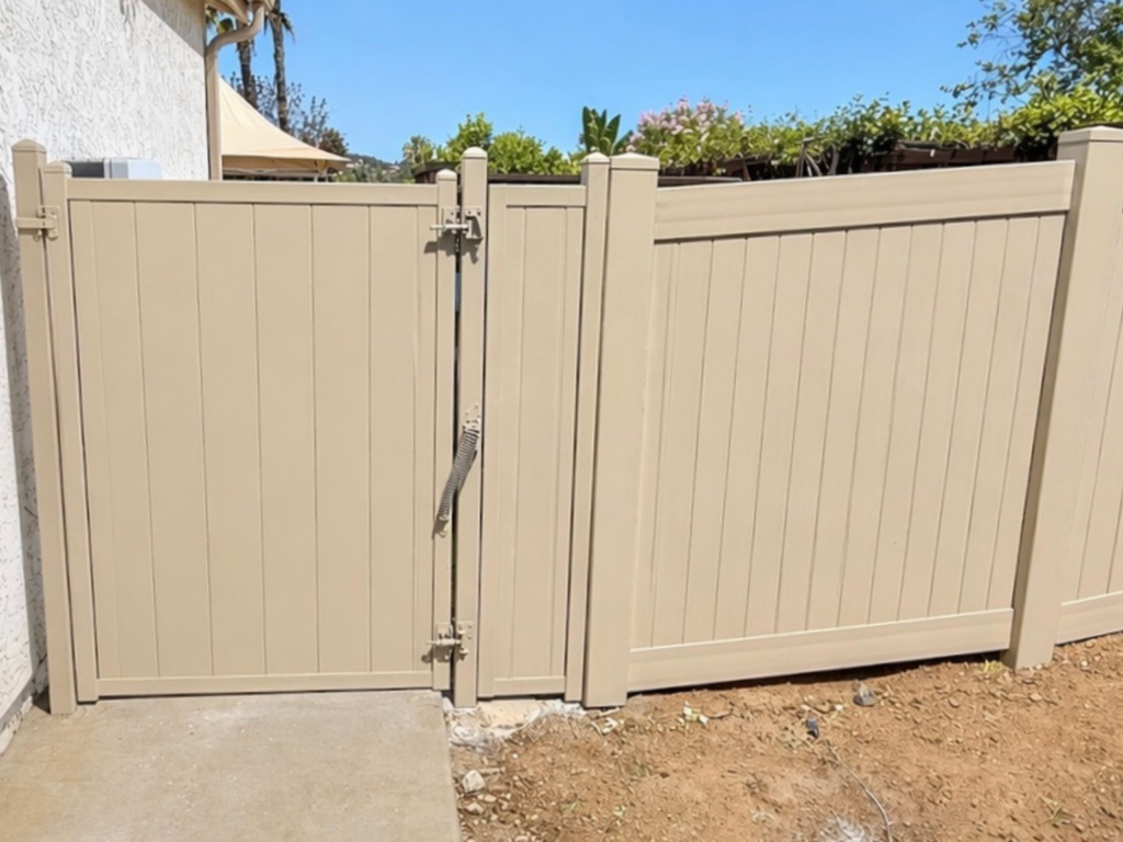 Tan metal privacy fencing with a gate on the side of a home.